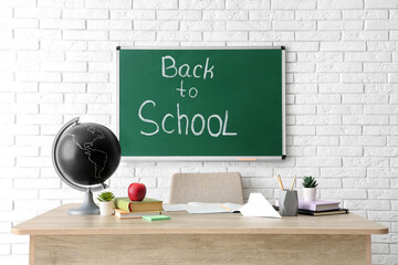 Poster - Apple, globe and stationery on teacher's desk in classroom. Back to school concept