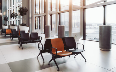 Wall Mural - A modern airport waiting area with rows of black and orange seats; potted plants and metal trash cans. Large windows allow natural light to flood the space, showcasing the view of the runway outside