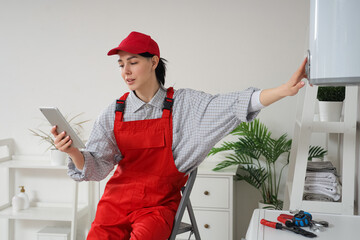 Wall Mural - Female worker with tablet computer adjusting modern electric boiler in bathroom