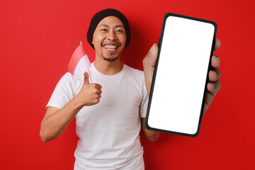 Indonesian man, with the Indonesian flag, shows a phone with an empty white screen while celebrating Indonesian Independence Day on August 17, Isolated on a red background