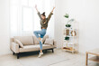 © SHOTPRIME STUDIO - Joyful woman dancing and jumping on the sofa at home, surrounded by music and happiness
