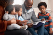 © peopleimages.com - Black family, book and man reading on sofa for storytelling, comic or development at home. Parents, children or dad with old yearbook on couch for joke, history or showing kids memories with care