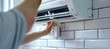 © Anoo - A close-up shot of a technician's hands carefully cleaning the fresh air grille of a mini-split system, the white tiled wall behind adding a clean and professional ambiance