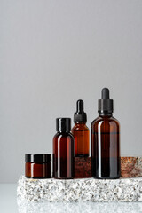 Wall Mural - Set of brown glass bottles with essential oils on stand on gray background