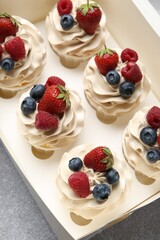 Wall Mural - Tasty cupcakes with different berries in box on light grey table, above view