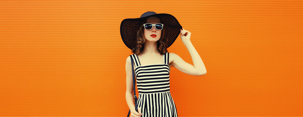 Wall Mural - Summer portrait of beautiful stylish young woman posing in hat, glasses on bright orange background