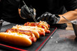 © pavel siamionov - Close-up of hands preparing hot dogs with various toppings.