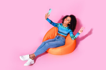 Sticker - Full size photo of pretty young girl sit orange beanbag selfie photo v-sign wear trendy blue outfit isolated on pink color background