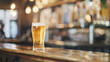 © Bonsales - Glass of cold beer with foam head on wooden bar counter in cozy pub with warm lighting. Blurred background of pub interior highlighting inviting and relaxing atmosphere