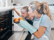 © Maass/peopleimages.com - Mom, oven and daughter in kitchen, smell and teaching of child of baking, recipe and muffins in home. Happy, girl and woman with gloves, smile and family with dessert, cupcakes and love for food