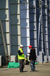 © Avatar_023 - Two multiracial construction workers or engineers walking side by side through a construction site, conversing.