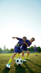 Boys in purple soccer uniforms competing for control of ball during game, showcasing competitive spirit. Vertical image. Concept of sport, childhood, education, achievement, active lifestyle