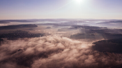 Sticker - Aerial view of rolling hills covered with dense mist and a bright sun in the morning sky