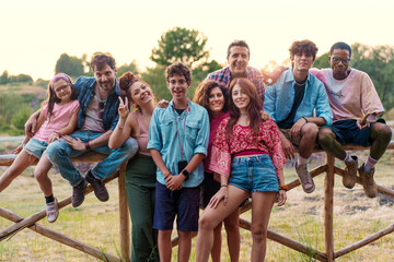 Diverse group of friends enjoying summer outdoors, multicultural family bonding on wooden fence in nature, inclusive community concept