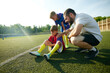 © master1305 - Coach providing assistance to child, boy sitting on field and feeling pain on legs, being injured during game. Concept of sport, childhood, education, achievement, active lifestyle