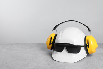 Sticker - Hard hat with earmuffs and goggles on gray surface against light background, space for text