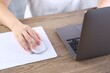 © New Africa - Woman using computer mouse while working with laptop at wooden table, closeup