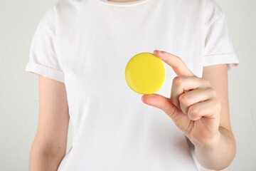 Wall Mural - woman with blank yellow button badge on light background, closeup