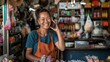 © OMD - Cheerful woman talking on smartphone in a vibrant, small shop, wearing an apron, surrounded by various merchandise and goods on shelves.