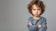 © TensorSpark - An angry little boy stands with a furious expression, arms crossed. The background is plain, providing ample space for copy text.