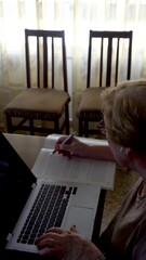 Canvas Print - Senior woman studying with a laptop and a book at home. Real time video.