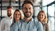© Alex - Confident business leader smiling with team members in blurred background, representing teamwork and leadership in a professional setting.