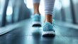 © Maximages  - A close-up image of someone’s feet, wearing blue athletic shoes, walking on a treadmill at the gym, capturing the motion and focus of exercise and fitness routine.