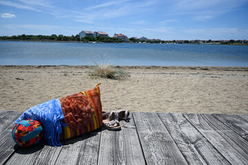 Summer accessories are sitting on a wooden dock with a beach bag in the background