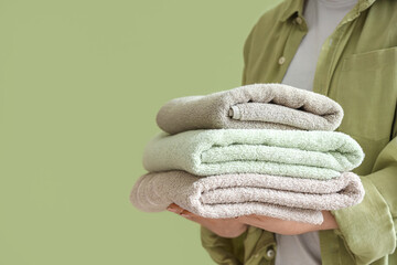 Wall Mural - Woman holding stack of clean soft towels on green background