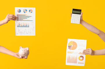 Wall Mural - Female hands with financial graphics, calculator and piggy bank on yellow background