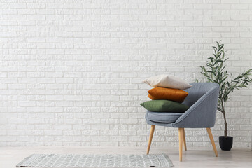 Canvas Print - Armchair with cushions and decorative olive tree near white brick wall