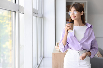 Wall Mural - Young woman in eyeglasses with cup of coffee near window at home