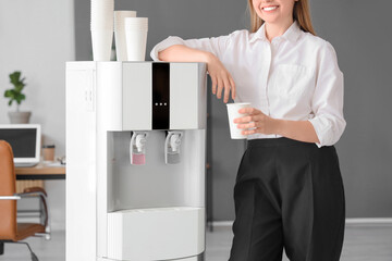 Wall Mural - Businesswoman with cup near water cooler in office