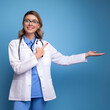 © efren - Fotografía de una doctora señalando con sus manos a la izquierda mientras esta de pie con vista frontal y alegre