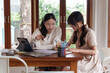 © Pichsakul - Two college friends are sitting at a wooden table, studying together