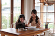 © Pichsakul - Two college friends are sitting at a wooden table, studying together