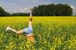 © Anton Belovodchenko - An adult happy woman in a red top and denim shorts jumps and makes a wheel element in a yellow rapeseed field. Motion blur effect.
