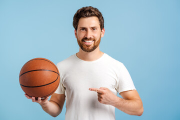 Wall Mural - Smiling young man holding basketball ball pointing with hand and finger