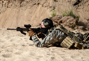 Wall Mural - A soldier in camouflage shoots from a machine gun while lying on the sand