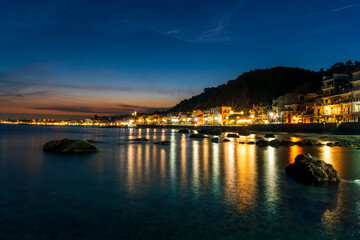 Wall Mural - night town coast with flashlights from embarkment and reflection in sea gulf water with golden urbal lights and blue hour sky on background of landscape