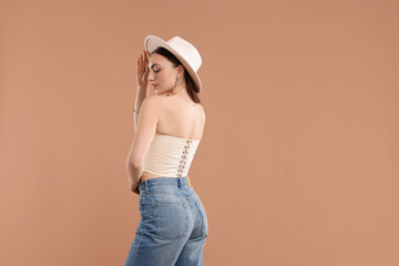 Wall Mural - Beautiful woman in stylish corset and hat posing on beige background. Space for text