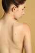 © New Africa - Woman with moles on her skin against beige background, back view