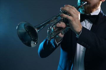 Professional musician playing trumpet on dark background, closeup