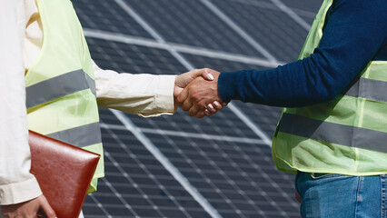 Wall Mural - Close up of handshake on solar panel background outside. Female engineer shakes hands with partner in agreement.