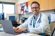 © Cetin - doctor sitting at his desk with a laptop, smiling and wearing a white coat and stethoscope in a medical office