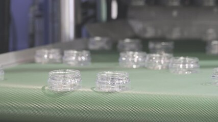 Poster - A moving conveyor belt with many clear plastic containers jars for cosmetics on it. The containers are being made in a factory
