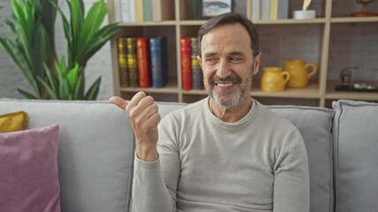 Canvas Print - Middle age hispanic man wearing sweater smiling with happy face looking and pointing to the side with thumb up. at home