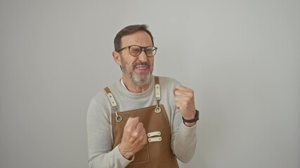 Poster - Joyful, middle age man celebrating a victorious moment, wearing apron, arms raised in triumph saying yes! standing isolated on white background, basking in success!