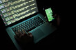 © JorSons/peopleimages.com - Laptop, cellphone and hands for hacker, coding or scam or fintech for cyber security. Dark, software or online crime for data programmer person, digital or thief on internet with typing or ransomware