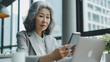 © iamfrk7 - Senior middle aged Asia businesswoman manager ceo using smartphone and laptop in office working online